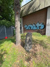 A brick building in Germany with a graffiti on the wall, a tree and grass in the foreground