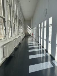 a long straight black-and-white hallway with windows to the left side and light reflections on the walls